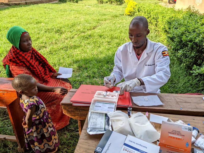 A MANCO clinician in a white coat sees a mother and her small daughter at an outdoor desk
